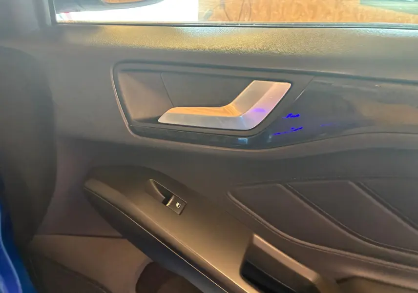 Détail de la porte intérieure côté gauche de la Ford Focus 2024 bleue, avec poignée argentée et commande de fenêtre.