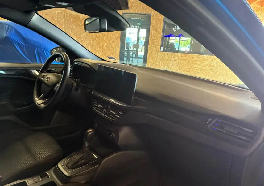 Vue intérieure côté conducteur de la Ford Focus bleu 2024, montrant le tableau de bord et la console centrale avec écran tactile.