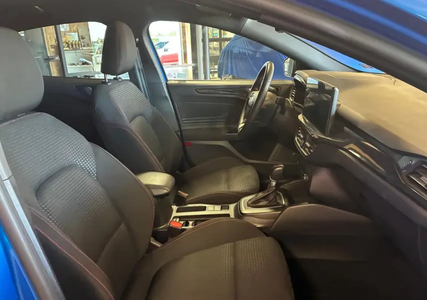 Vue intérieure côté gauche de la Ford Focus bleu 2024, montrant les sièges avant noirs et la console centrale avec boîte auto.