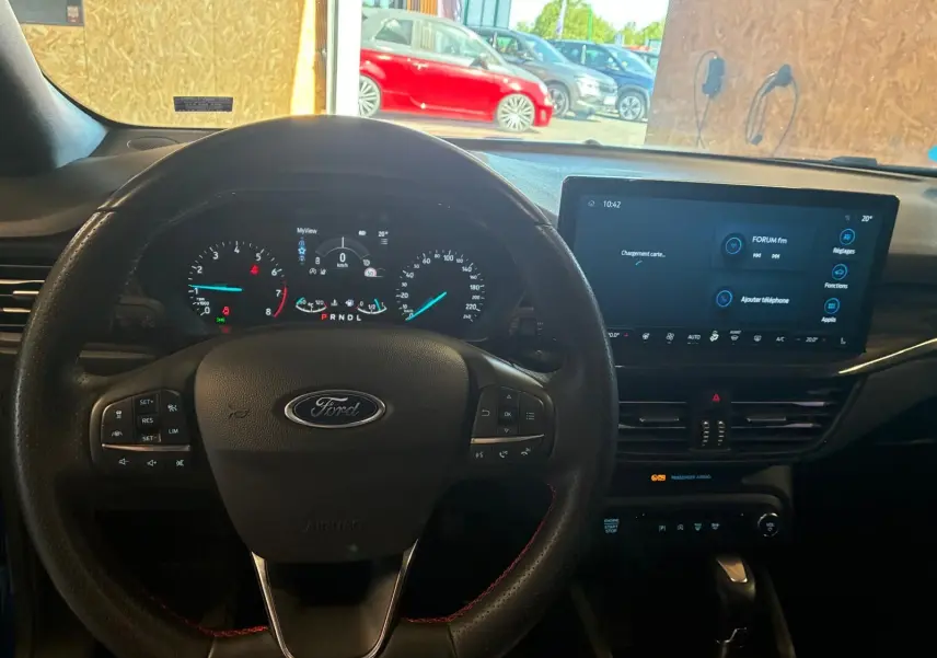 Vue intérieure centrée sur le volant Ford et le tableau de bord numérique d'une Focus 2024, avec écran tactile et commandes au volant.