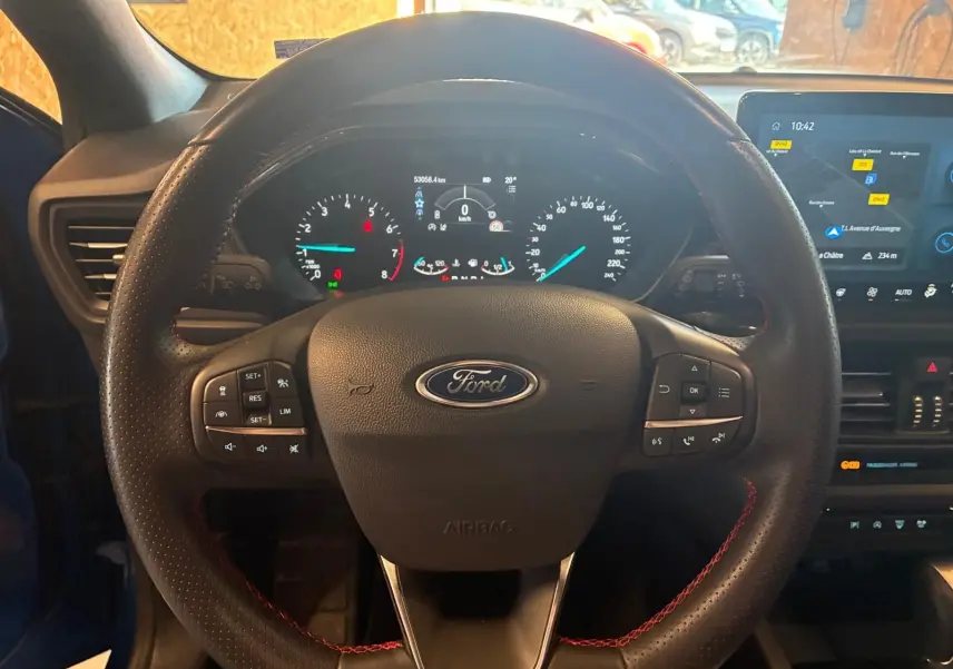 Vue centrée sur le volant noir avec surpiqûres rouges de la Ford Focus bleu 2024, tableau de bord et écran tactile visibles.
