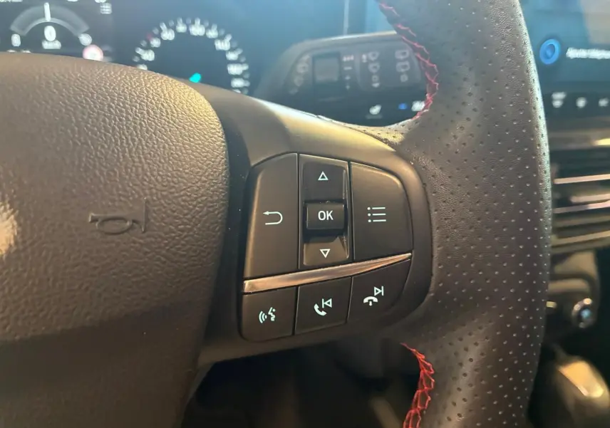 Gros plan sur les commandes au volant en cuir noir perforé avec surpiqûres rouges de la Ford Focus 2024.