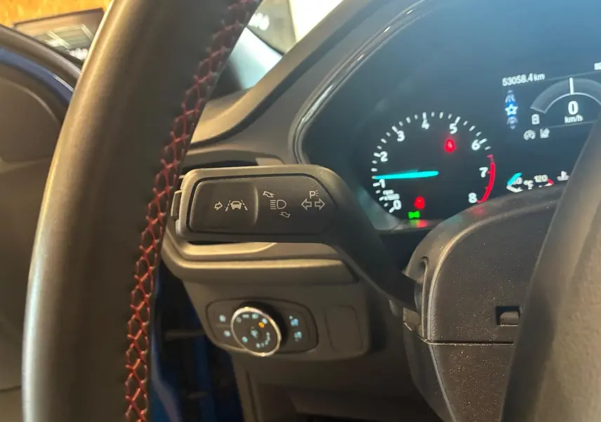 Vue intérieure rapprochée du levier de clignotant et du tableau de bord numérique d'une Ford Focus bleue 2024.