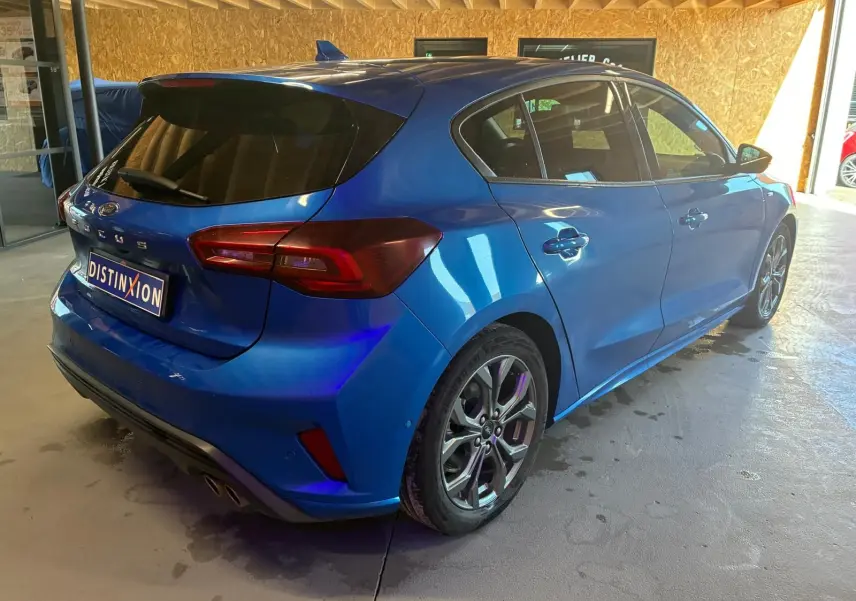 Ford Focus bleu vue 3/4 arrière droit en intérieur, avec jantes alliage et vitres teintées.