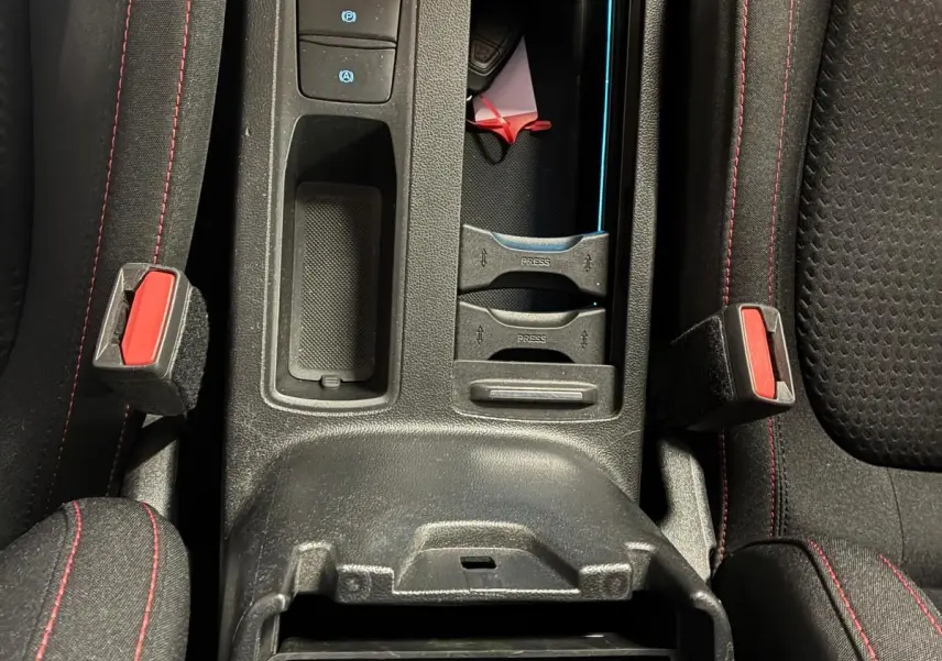 Vue plongeante sur la console centrale noire de la Ford Focus 2024, avec surpiqûres rouges et rangements ouverts.