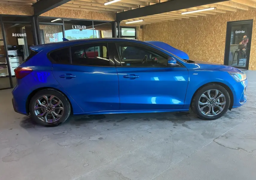 Vue de profil côté gauche d'une Ford Focus 2024 bleu vif, finition ST Line avec jantes alliage et cinq portes.