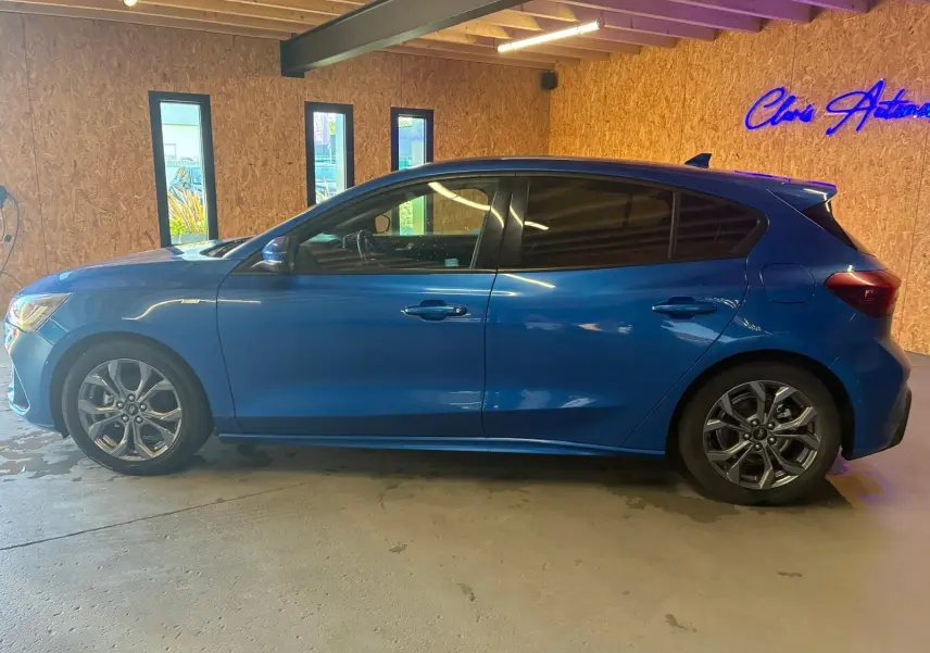 Vue de profil côté gauche d'une Ford Focus bleu 2024 ST Line avec jantes alliage et vitres teintées, stationnée en intérieur.