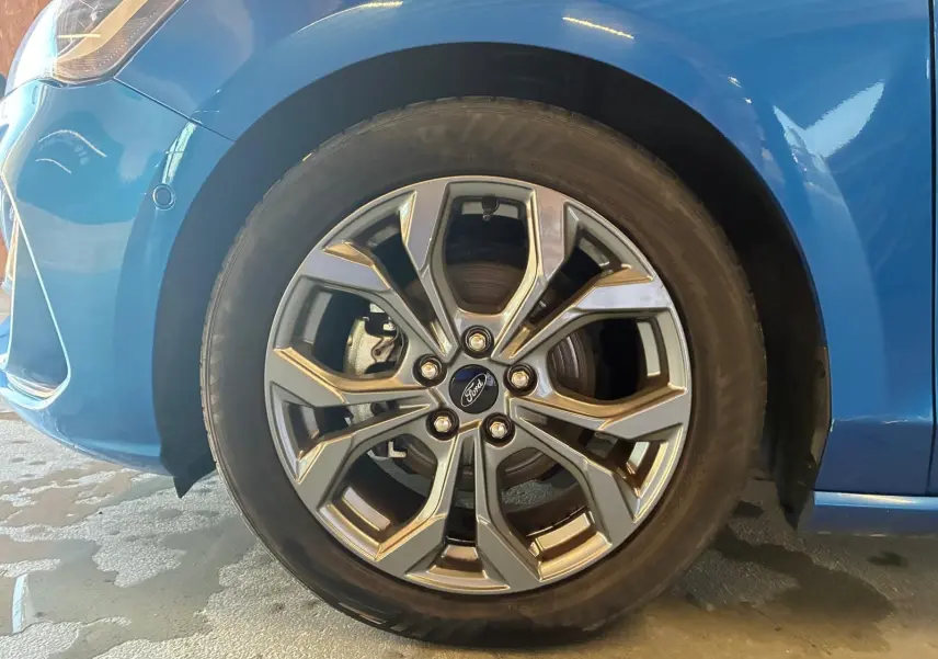 Gros plan sur la roue avant gauche d'une Ford Focus bleue 2024, mettant en valeur la jante alliage au design moderne.