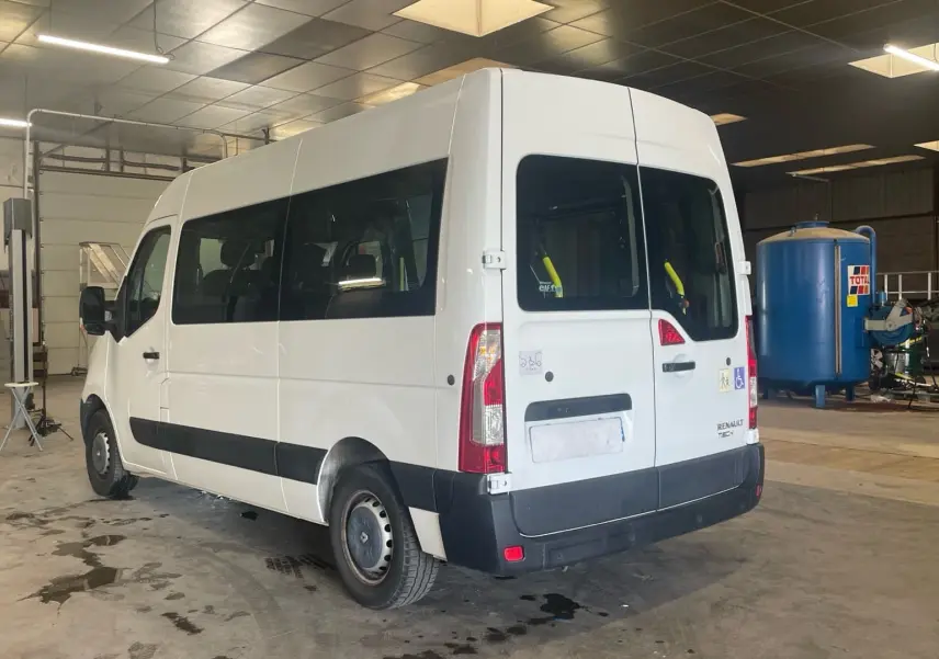 Renault Master blanc vu en 3/4 arrière droit dans un atelier, avec rampe arrière et vitres latérales teintées.
