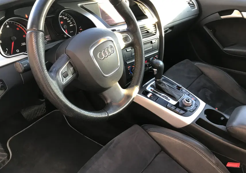 Intérieur noir de l'Audi A5 2012, vue côté conducteur sur le volant, tableau de bord et console centrale avec boîte auto.