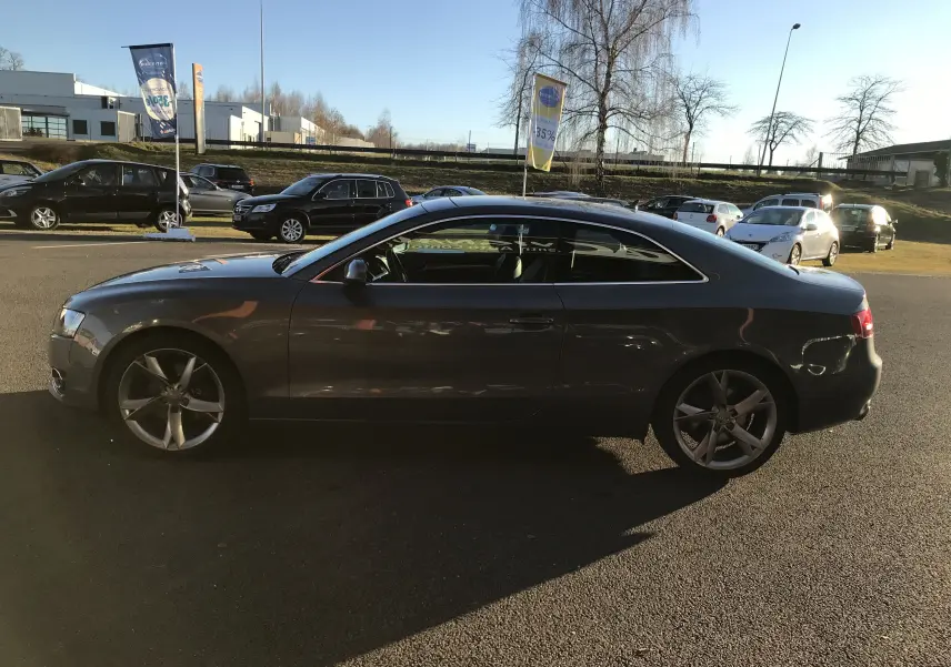 Audi A5 Coupé gris dauphin vu de profil côté gauche, avec jantes alliage et lignes élégantes.
