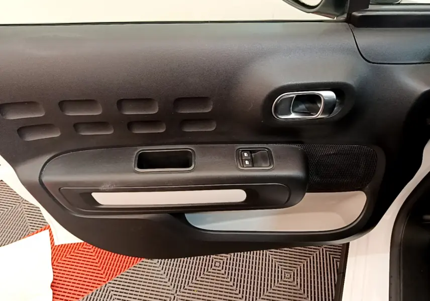 Gros plan sur la porte côté droit de la Citroën C3 blanche, montrant la poignée intérieure et les commandes des vitres.