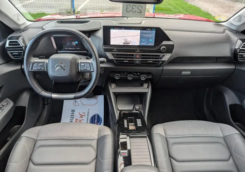 Intérieur de la Citroën C4 2024 vu de face, tableau de bord moderne avec écran tactile central et sièges gris tissu et cuir.