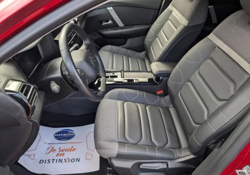 Vue intérieure côté conducteur de la Citroën C4 2024 rouge foncé, sièges Advanced Comfort gris et volant cuir noir.