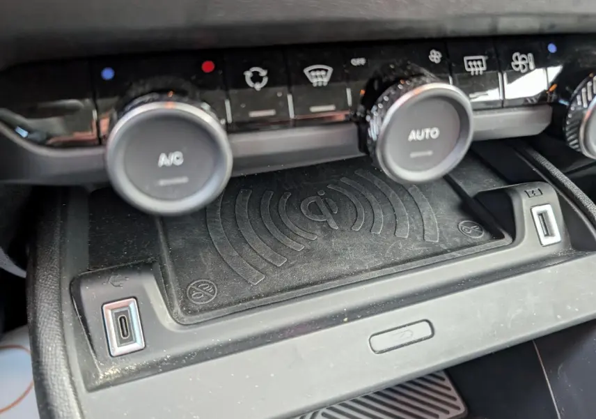 Gros plan sur la console centrale noire du Citroën C4 2024, montrant la recharge sans fil Qi et commandes climatisation.