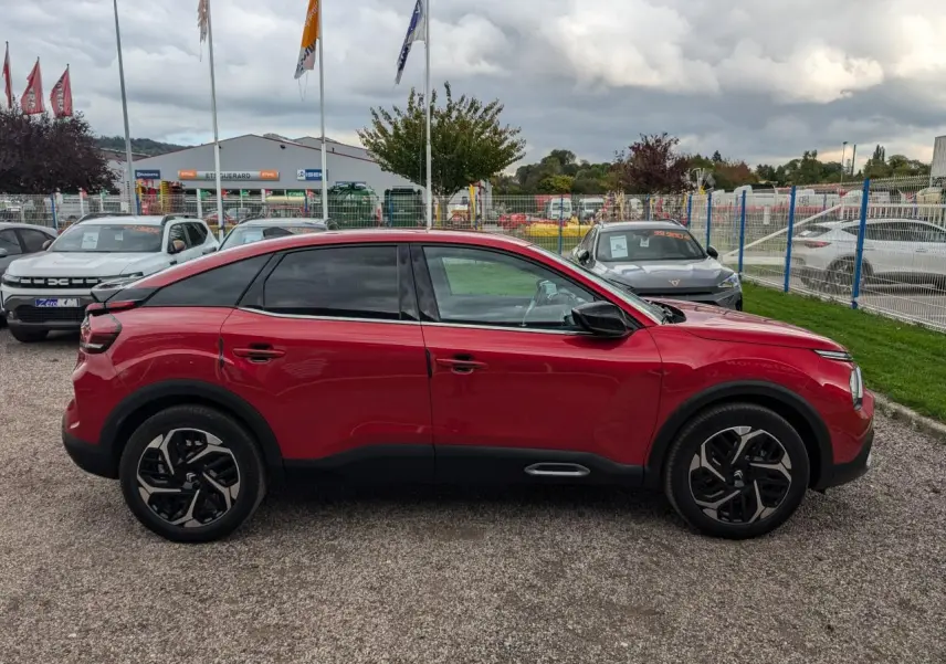 Profil côté gauche d'une Citroën C4 2024 rouge foncé avec jantes alliage noires et vitres surteintées.