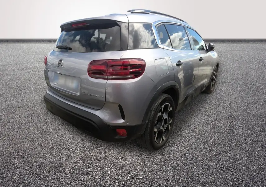 Vue 3/4 arrière droit d'un Citroën C5 gris clair hybride 2024 avec toit noir et jantes noires distinctives.