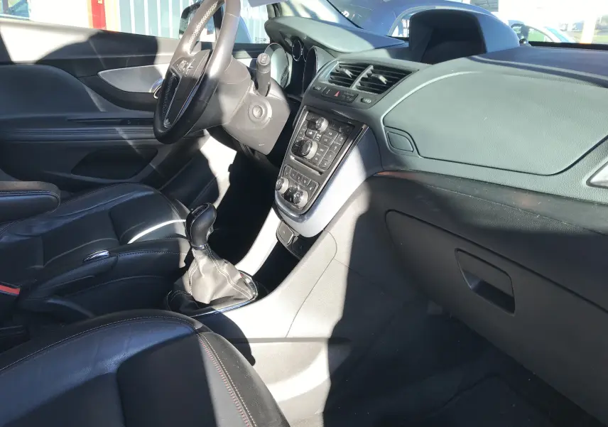 Vue intérieure côté conducteur de l'Opel Mokka blanc 2015, montrant le tableau de bord et les sièges en cuir noir.