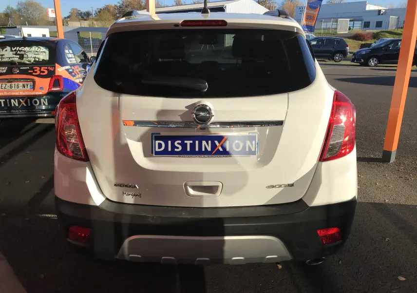 Vue arrière d'un Opel Mokka blanc 2015 avec logo et plaque Distinxion, feux rouges et lunette arrière teintée.
