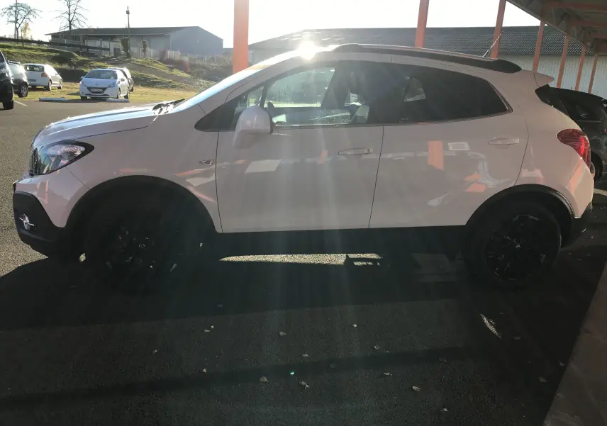 Opel Mokka blanc vue de profil côté gauche, avec jantes noires et toit ouvrant sous un abri.