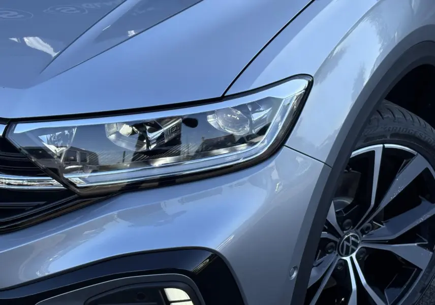 Gros plan sur l'avant droit du Volkswagen T-Roc gris pyrite, mettant en valeur le phare LED et la jante alliage 19 pouces.