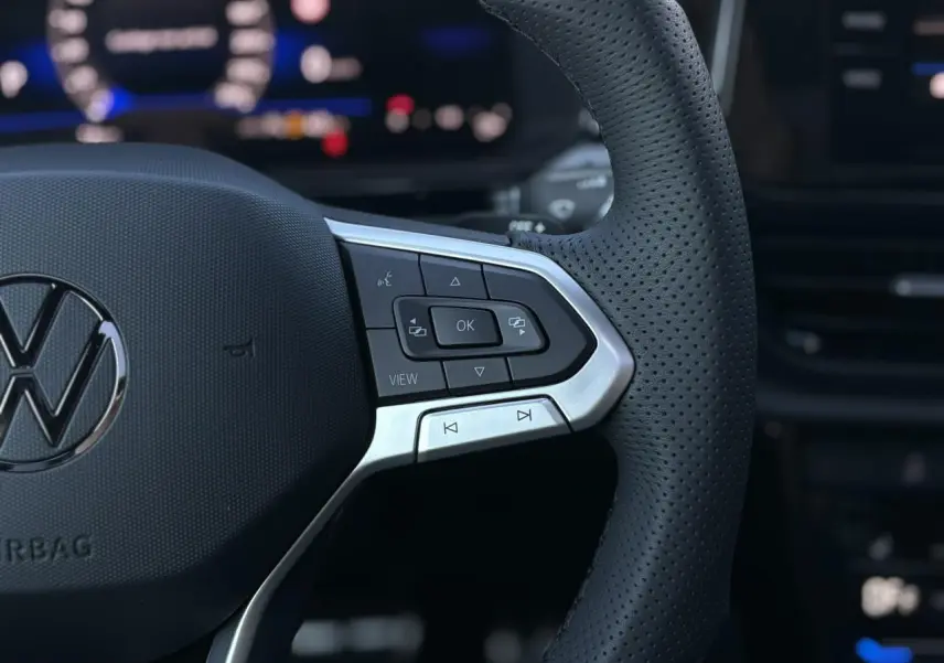 Gros plan sur le volant en cuir perforé du Volkswagen T-Roc 2025 avec commandes multifonctions et logo VW central.