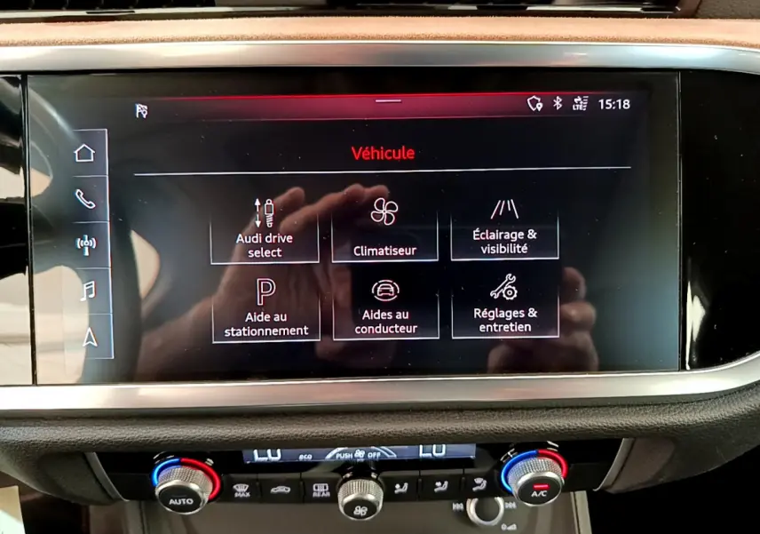 Écran tactile central de l'Audi Q3 bleu 2020 affichant les options de conduite et d'aide au stationnement.