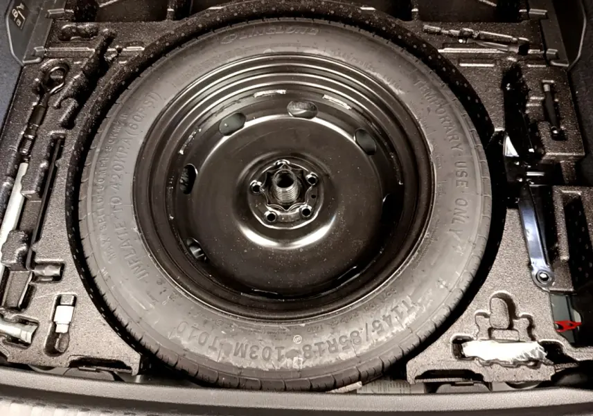 Gros plan sur la roue de secours noire dans le coffre de l'Audi Q3 bleu 35 TDI 2020, entourée des outils de bord.