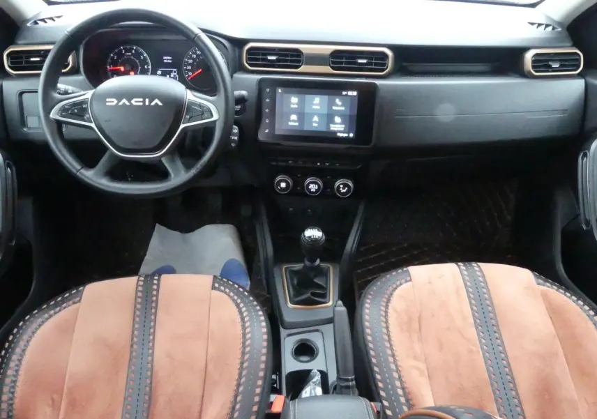Vue intérieure avant du Dacia Duster 2023 avec volant noir, tableau de bord moderne et sellerie brun cuivré spécifique Extreme.