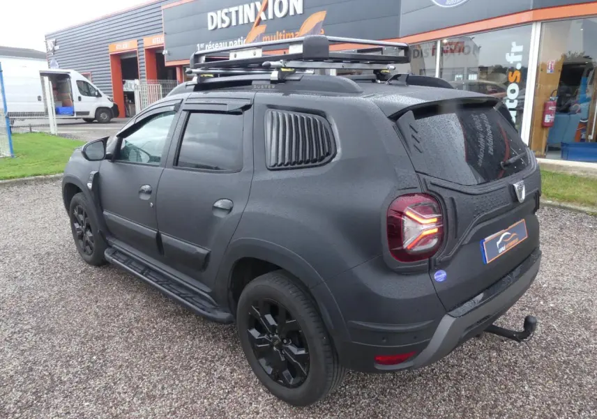 Vue 3/4 arrière droite du Dacia Duster noir 2023 avec covering intégral, galerie de toit et attelage fixe.