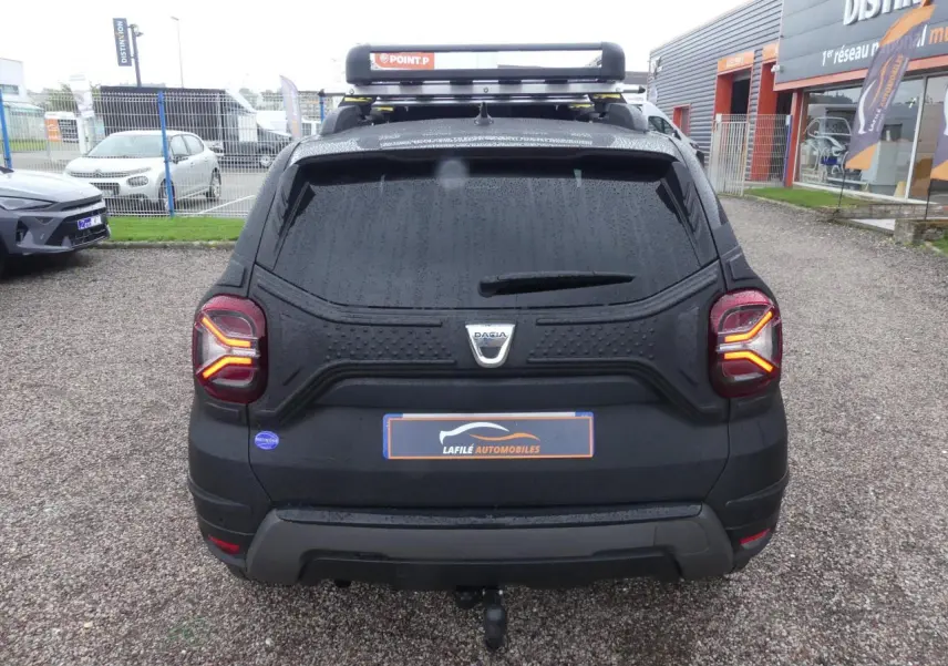 Vue arrière d'un Dacia Duster noir 2023 avec attelage fixe et galerie de toit, vitres arrière surteintées.