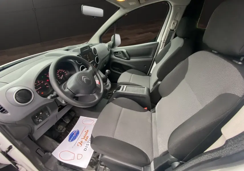 Vue intérieure côté conducteur du Citroën Berlingo blanc 2018, montrant le tableau de bord et les sièges avant gris et noirs.