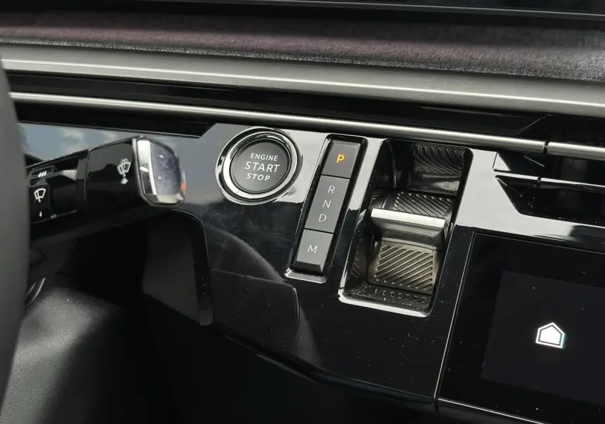 Gros plan sur la console centrale noire brillante du Peugeot 3008 Hybrid 145 avec bouton start/stop et commande de boîte automatique.