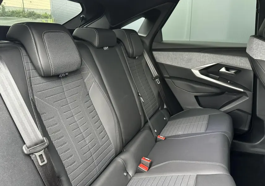 Vue latérale droite des sièges arrière noirs et gris du Peugeot 3008 Hybrid 2024 avec surpiqûres blanches et ceintures visibles.