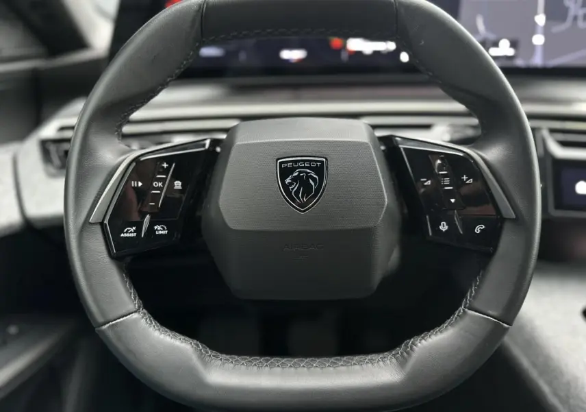 Volant compact cuir noir avec logo Peugeot au centre, vue rapprochée de l'intérieur du 3008 Hybrid 2024.