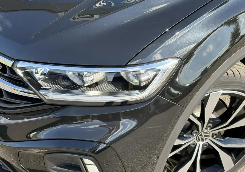 Gros plan sur l'avant droit noir Grenadilla du Volkswagen T-Roc 2025 avec projecteur LED et jante alliage R-Line.