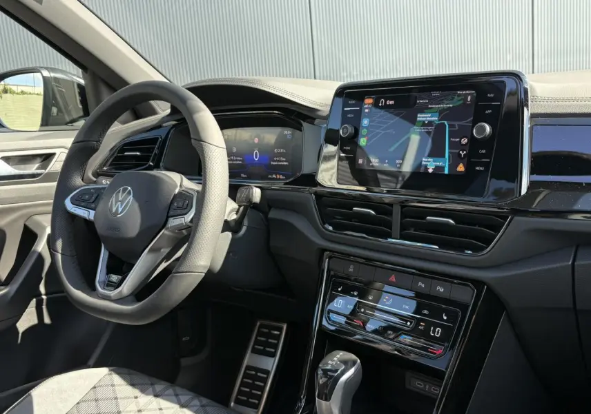 Intérieur du Volkswagen T-Roc 2025 vu côté conducteur, volant cuir avec logo VW et écran tactile de navigation allumé.