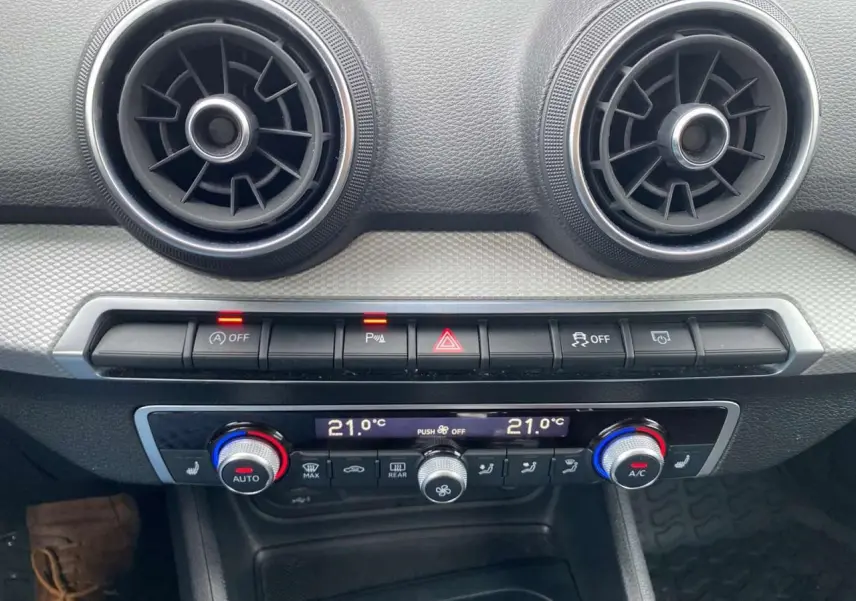 Détail de la console centrale de l’Audi Q2 noire 2023, avec commandes climatisation automatique et aérateurs ronds.