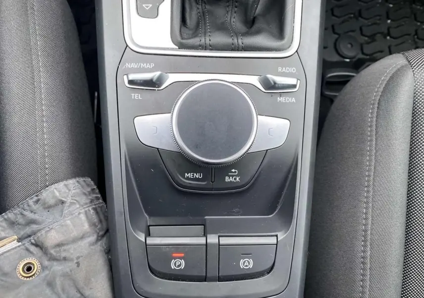Vue plongeante sur la console centrale noire de l'Audi Q2 2023, avec molette MMI et commandes électroniques visibles.