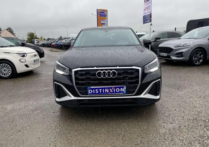 Vue avant d’un Audi Q2 noir 2023 avec calandre large, phares allumés et pluie visible sur la carrosserie.