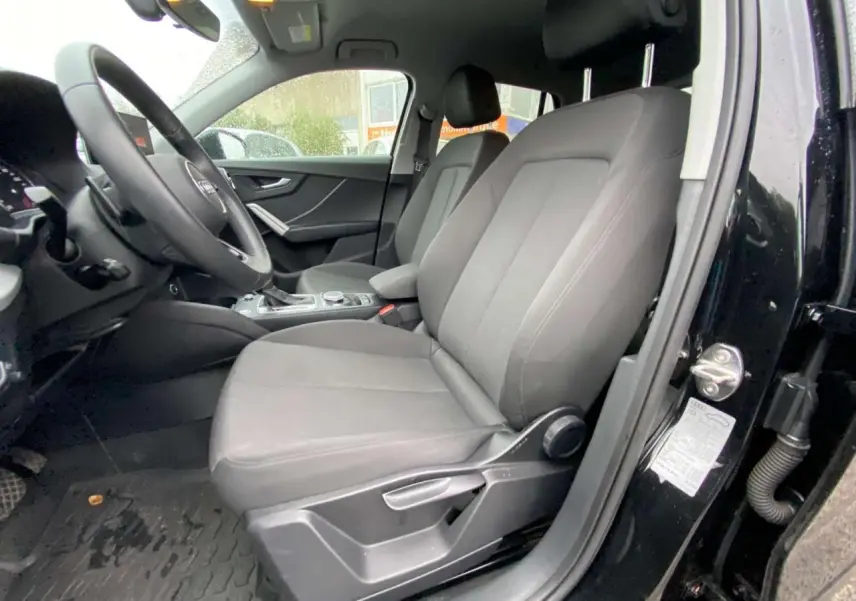 Vue intérieure côté conducteur d'un Audi Q2 noir 2023, sièges avant en tissu gris et tableau de bord visible.
