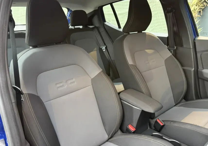 Vue intérieure montrant les sièges avant gris avec logo DC embossé et accoudoir central de la Dacia Sandero Stepway Bleu Iron.