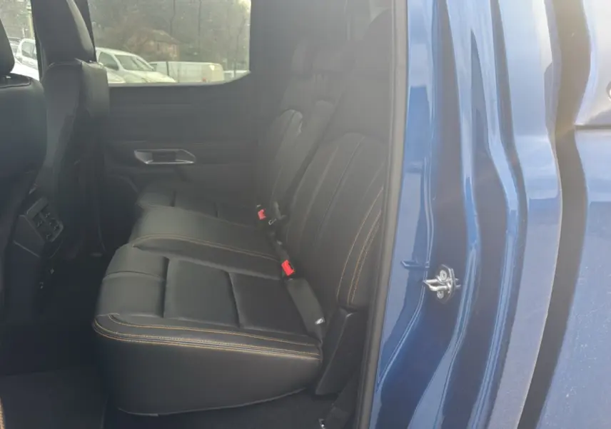 Vue intérieure côté arrière droit du Ford Ranger 3.0 V6 Wildtrak bleu lightning, sièges cuir noirs avec surpiqûres orange.