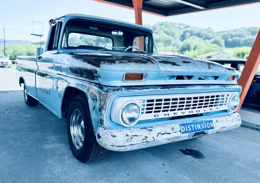 Vue 3/4 avant d’un Chevrolet C10 Apache 1963 bleu avec carrosserie patinée et pare-chocs usé sous abri.