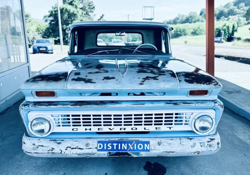 Vue frontale d’un Chevrolet C10 Apache 1963 bleu avec capot patiné et pare-chocs usé visible en stationnement.