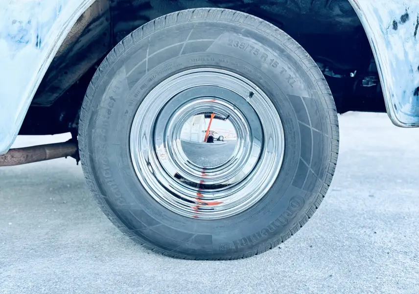 Gros plan sur la roue arrière droite chromée du Chevrolet C10 Apache 1963 bleu, avec partie de la carrosserie visible.