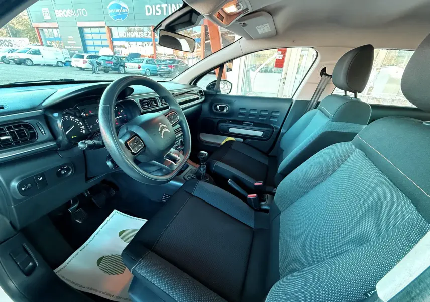 Intérieur de la Citroën C3 blanc, vue côté conducteur, montrant le volant, tableau de bord et sièges noirs et gris.