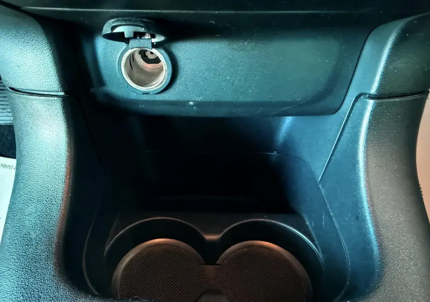 Prise allume-cigare ouverte et porte-gobelets noirs au centre de la console d'une Citroën C3 blanche de 2021.