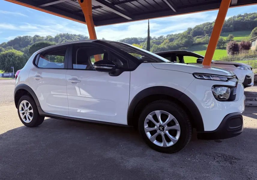 Vue latérale côté gauche d'une Citroën C3 blanche stationnée sous un abri avec des montants orange.