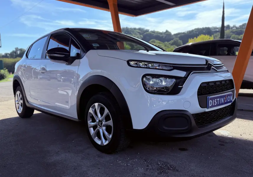 Citroën C3 blanc vue 3/4 avant droit sous abri, avec calandre noire et jantes argentées.